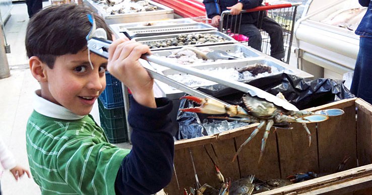 A young shopper holding up a live blue crab with tongs